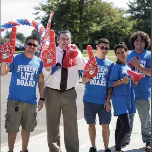 President Stout with four students holding number #1 red foam fingers.