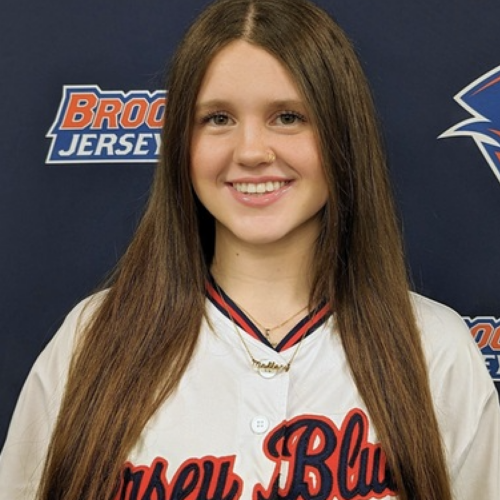 Woman with long brown hair wearing a softball jersey.