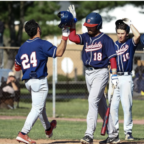Three baseball players at home plate. Two are giving each other a high-five.