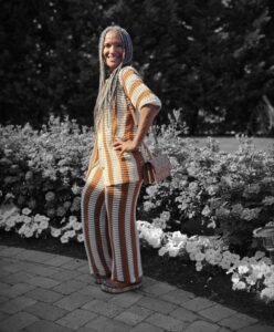 A beautiful woman with dark skin and long braided hair wearing a gold and white striped top and pants.
