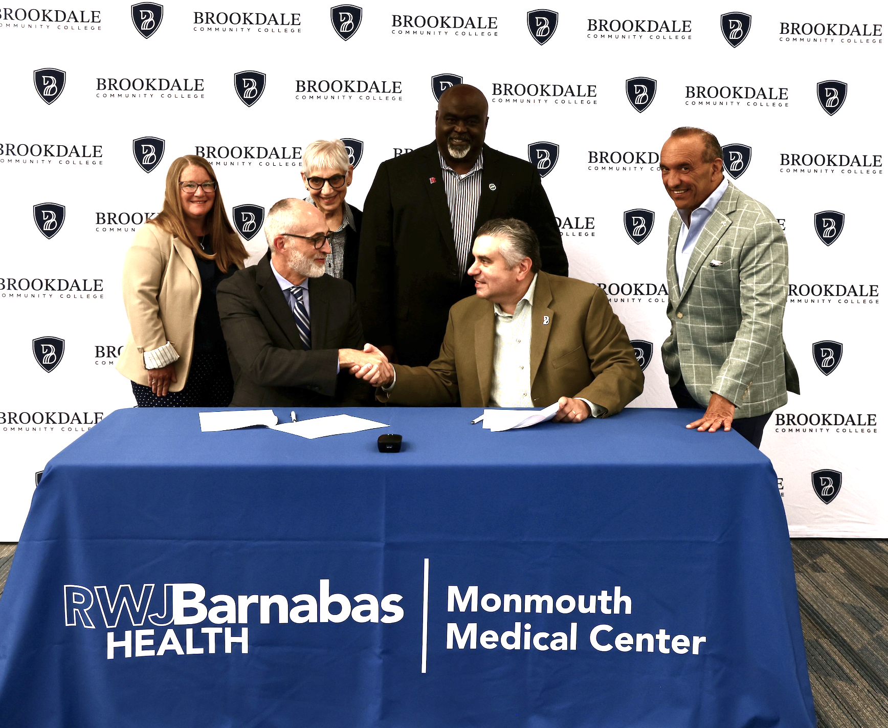 Eric Carney and David M. Stout shaking hands with Commissioner Director Thomas A. Arnone, Dr. Charles Ford, Dean Jayne Edman and Ann Szapor, Chief Nursing Officer, Monmouth Medical Center looking on.